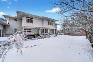 Snow covered rear of property with a patio area and stucco siding