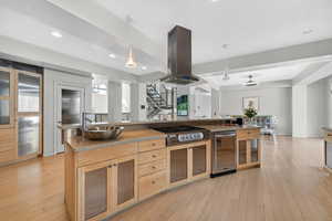Kitchen featuring glass fronted cabinets, island exhaust hood, hanging light fixtures, and light wood finished floors
