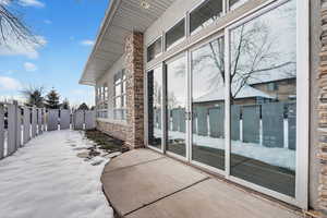 Snow covered property entrance featuring a gate, stone siding, and a patio