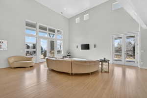 Living room with french doors, a high ceiling, light wood-type flooring, and healthy amount of natural light