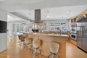 Kitchen with glass insert cabinets, light wood finished floors, stainless steel appliances, and a breakfast bar