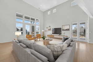Living room with french doors, light wood-style floors, a high ceiling, and plenty of natural light