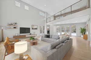 Living room featuring light wood-type flooring, recessed lighting, french doors, and a high ceiling