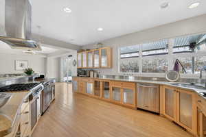 Kitchen with glass insert cabinets, island range hood, stainless steel appliances, decorative light fixtures, and light wood finished floors