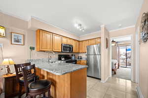 Kitchen with ornamental molding, stainless steel appliances, a peninsula, a ceiling fan, and baseboard heating