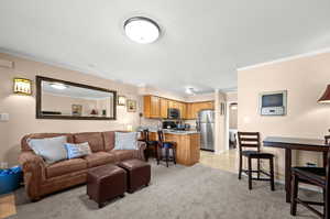Living area with crown molding, light colored carpet, and light tile patterned floors