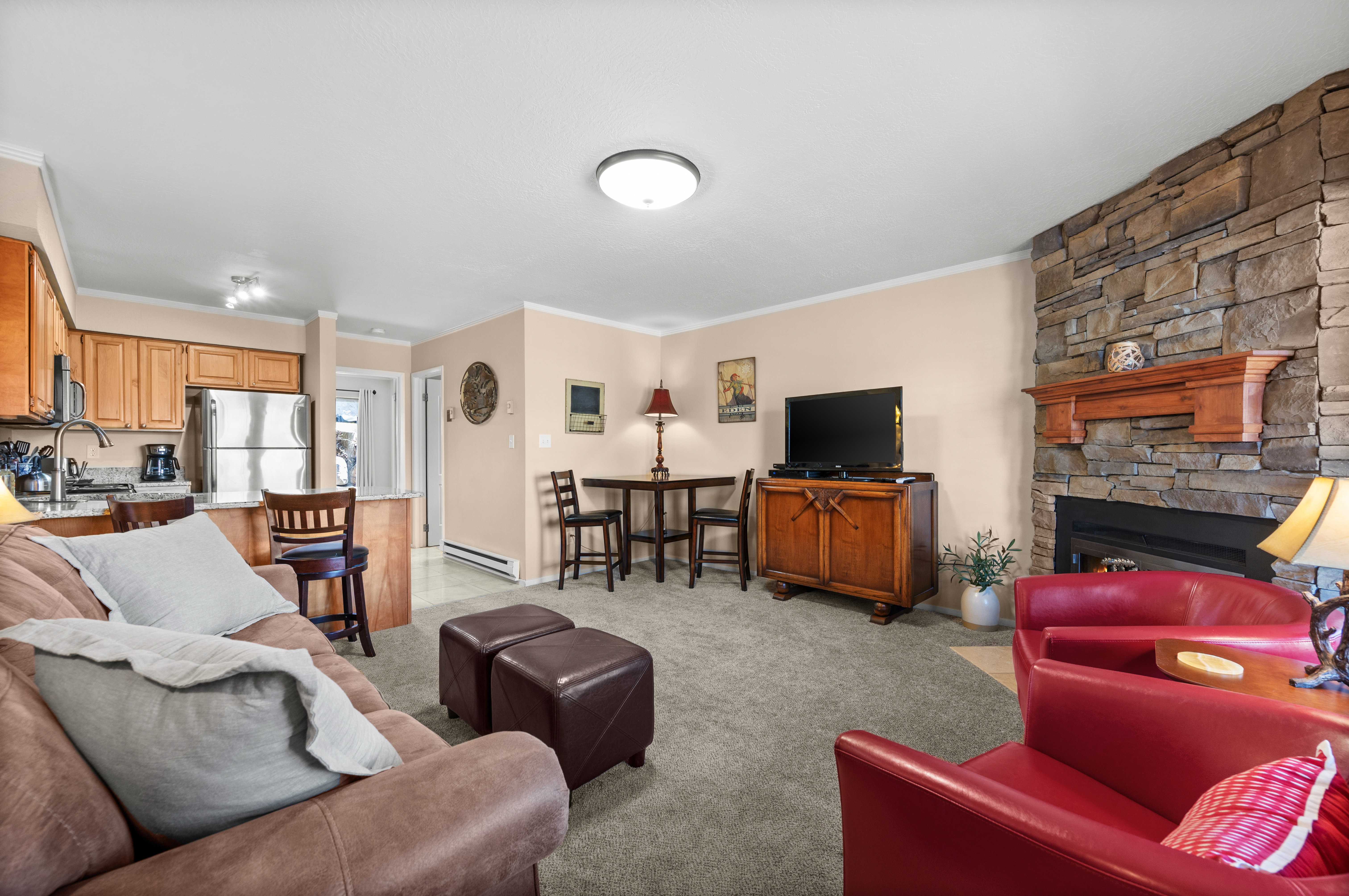 Living area featuring crown molding, light colored carpet, baseboard heating, and a stone fireplace