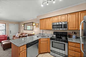 Kitchen with stainless steel appliances, a peninsula, open floor plan, healthy amount of natural light, and crown molding