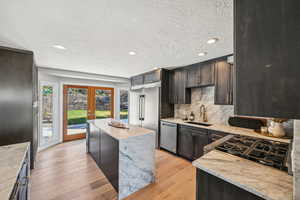 Kitchen featuring light stone counters, light wood-style floors, stainless steel appliances, a textured ceiling, and french doors