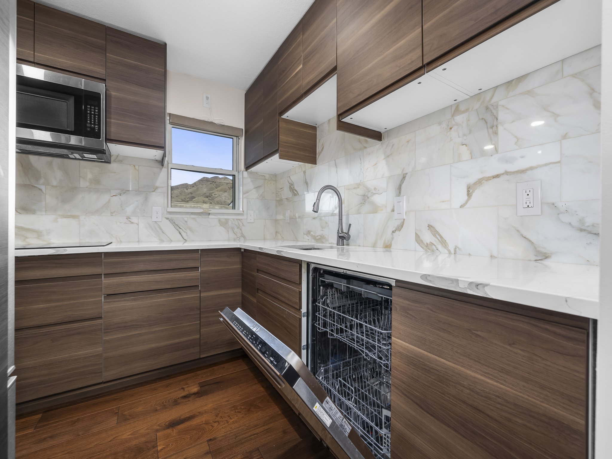 Kitchen featuring modern cabinets, light stone countertops, dark wood finish cabinetry, stainless steel microwave, and dark wood-style flooring