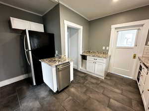 Kitchen featuring white cabinets, crown molding, light stone counters, stainless steel appliances, and decorative backsplash
