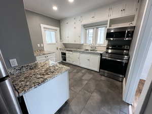 Kitchen with stainless steel appliances, white cabinetry, light stone counters, backsplash, and healthy amount of natural light