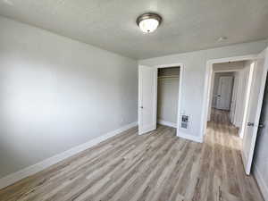 Unfurnished bedroom with light wood-type flooring, a closet, and a textured ceiling