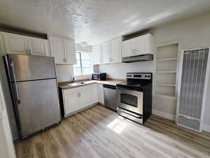 Kitchen with stainless steel appliances, a textured ceiling, a heating unit, white cabinets, and light wood-style floors