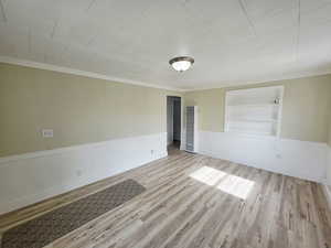 Spare room featuring built in features, light wood-style flooring, wainscoting, a heating unit, and crown molding