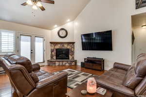 Living room featuring ceiling fan, french doors, vaulted ceiling, wood finished floors, and a fireplace