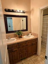 Full bath with double vanity, light tile patterned floors, and a shower with shower curtain