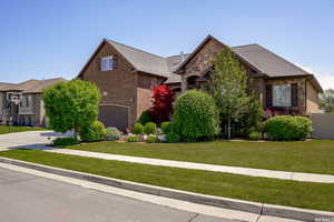 View of front facade with a front yard, stone siding, a garage, brick siding, and driveway