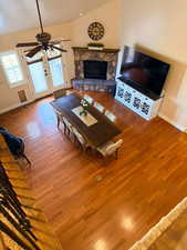 Living area with a stone fireplace, lofted ceiling, wood finished floors, and ceiling fan