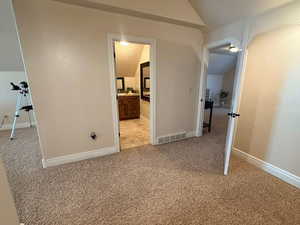 Unfurnished bedroom with light carpet, lofted ceiling, and ensuite bathroom