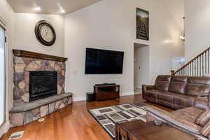 Living room with wood finished floors, a stone fireplace, and vaulted ceiling