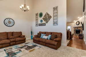 Living area featuring a high ceiling, a stone fireplace, carpet floors, and a chandelier