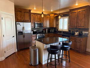 Kitchen with stainless steel appliances, a breakfast bar area, a kitchen island, a textured ceiling, and decorative light fixtures