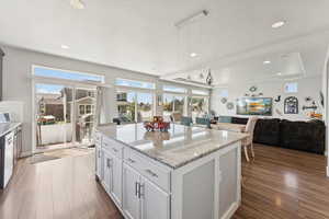Kitchen featuring open floor plan, light stone countertops, a center island, dark wood-style flooring, and decorative light fixtures