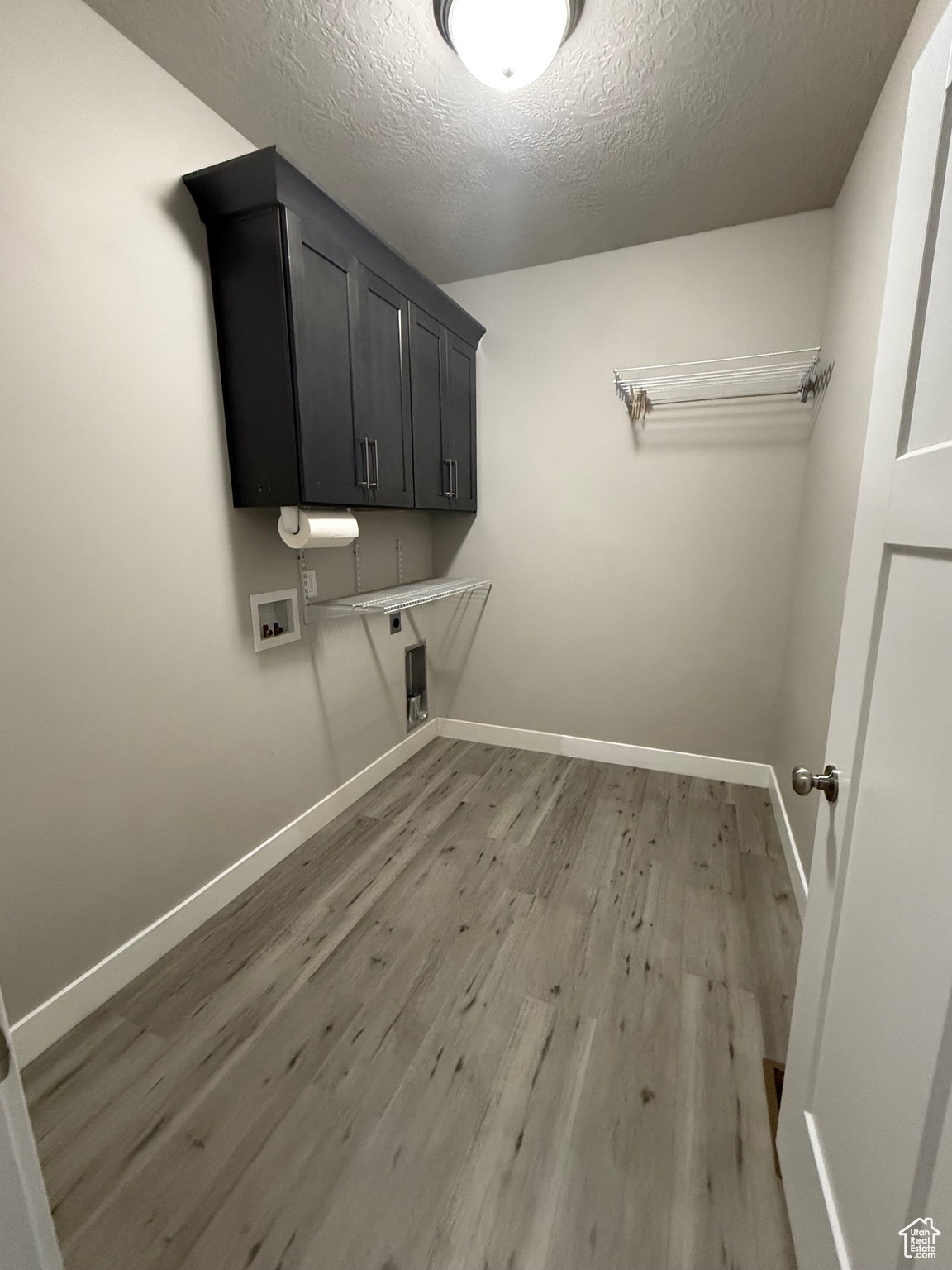 Laundry room with light wood-style floors, a textured ceiling, hookup for a washing machine, and cabinet space