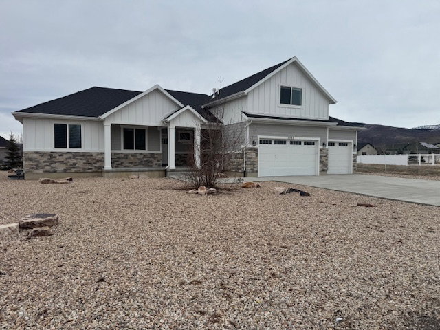 View of front of property featuring board and batten siding, an attached garage, a porch, stone siding, and concrete driveway