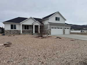 View of front of property featuring board and batten siding, an attached garage, a porch, stone siding, and concrete driveway