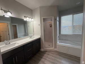 Bathroom featuring a garden tub, double vanity, a marble finish shower, and light wood-style floors