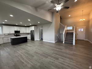 Dual tone kitchen with open floor plan, a center island, stainless steel appliances, ceiling fan, and light wood-style flooring