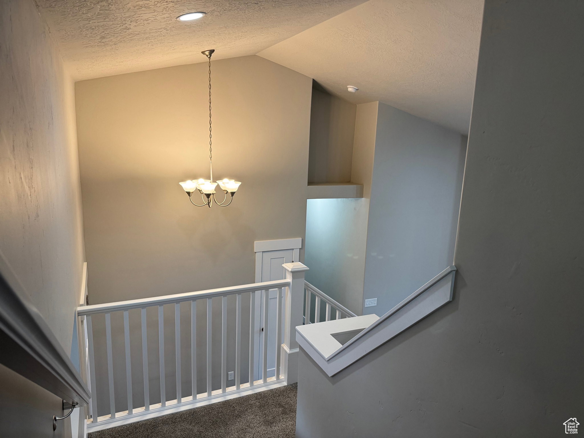 Staircase featuring a textured ceiling, carpet, and suspended lighting