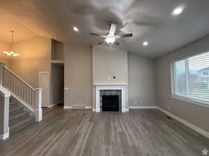 Unfurnished living room featuring a tiled fireplace, lofted ceiling, light wood-type flooring, ceiling fan, and suspended lighting