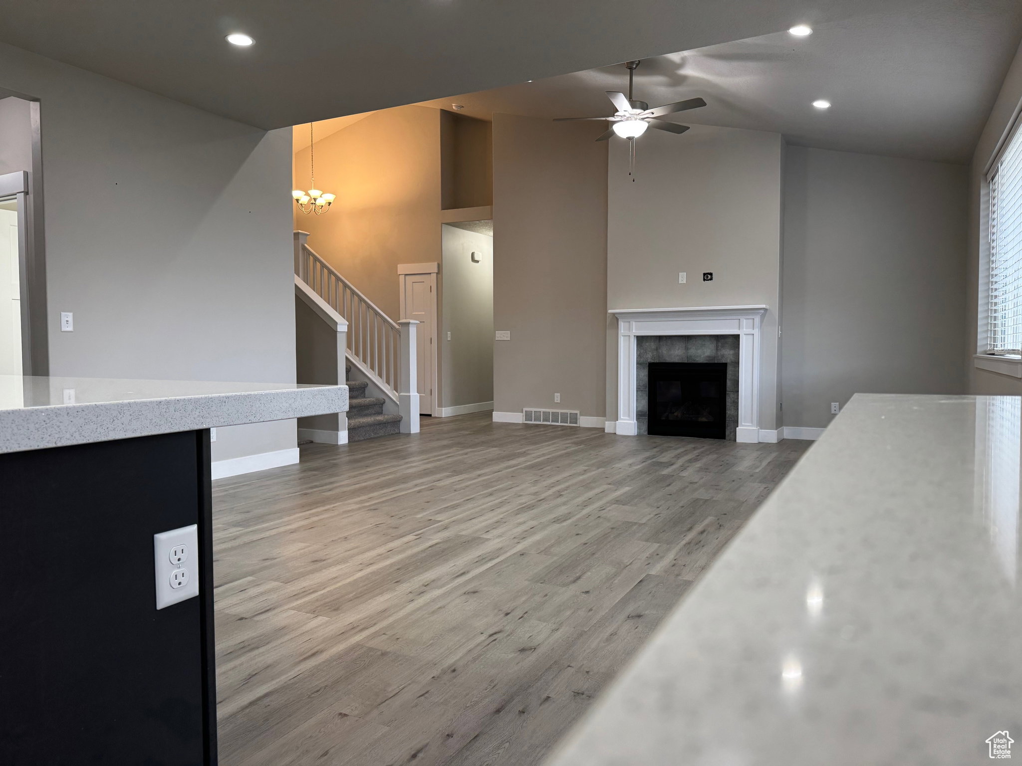 Unfurnished living room featuring light wood-style floors, a tiled fireplace, vaulted ceiling, a ceiling fan, and a chandelier
