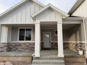 Doorway to property with board and batten siding, stone siding, and covered porch