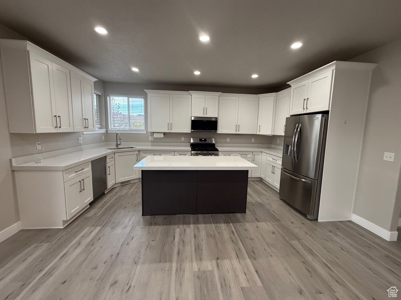 Two tone kitchen with stainless steel appliances, a center island, recessed lighting, light stone counters, and light wood finished floors