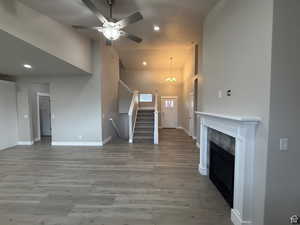Unfurnished living room featuring a high ceiling, light wood-style flooring, ceiling fan, suspended lighting, and a high end fireplace