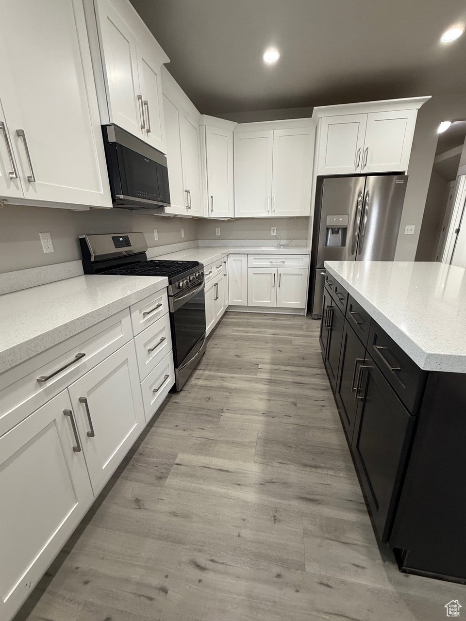 Kitchen featuring two tone color scheme, stainless steel appliances, light stone counters, recessed lighting, and light wood finished floors