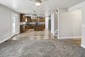Kitchen featuring a kitchen island, open floor plan, hanging light fixtures, light carpet, and stainless steel appliances