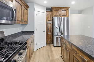 Kitchen featuring stainless steel appliances, light wood-style floors, recessed lighting, dark stone counters, and wood finish cabinets