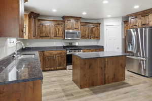 Kitchen with stainless steel appliances, a center island, recessed lighting, dark stone countertops, and light wood-type flooring