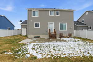 Snow covered back of property featuring a patio, a fenced backyard, entry steps, and stucco siding