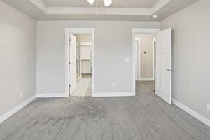 Unfurnished bedroom featuring light carpet, a raised ceiling, a walk in closet, and ceiling fan