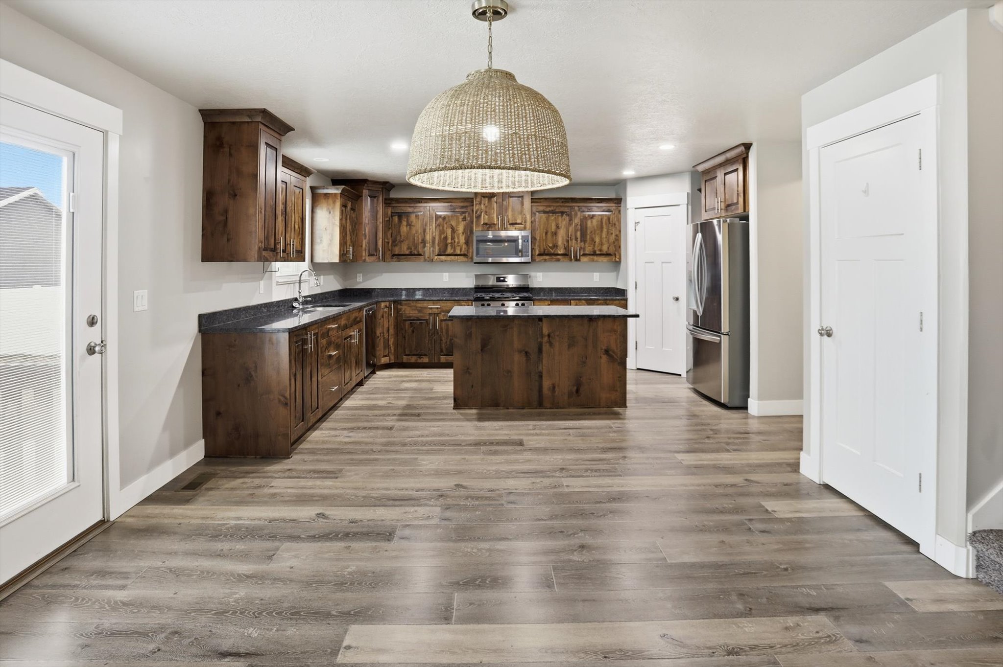 Kitchen with a center island, dark wood finish cabinets, stainless steel appliances, hanging light fixtures, and light wood-type flooring