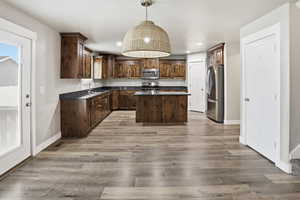 Kitchen with a center island, dark wood finish cabinets, stainless steel appliances, hanging light fixtures, and light wood-type flooring