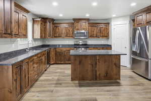 Kitchen featuring stainless steel appliances, dark stone counters, a center island, recessed lighting, and light wood-style flooring