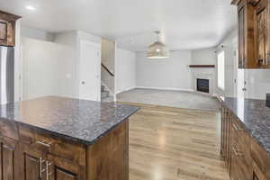 Kitchen featuring a tiled fireplace, dark stone countertops, open floor plan, light wood-style flooring, and pendant lighting