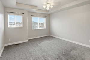 Spare room with a tray ceiling, light carpet, and ceiling fan